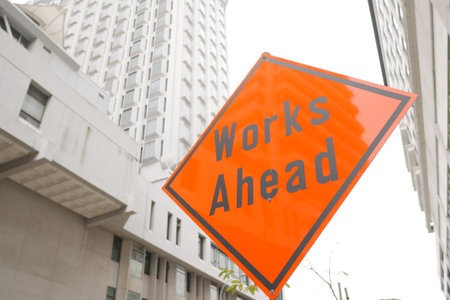 works ahead sign and buildings in singapore cityの写真素材