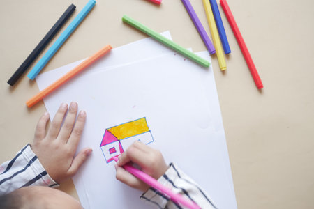 top view of child girl drawing a house with color pencils on paperの写真素材