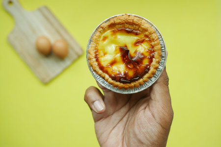 holding a a egg tart against yellow background