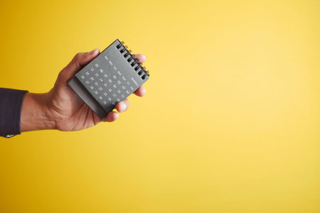 hand holding a calendar against yellow backgroundの写真素材