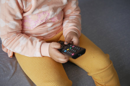 child holding a tv remote sitting on sofaの写真素材