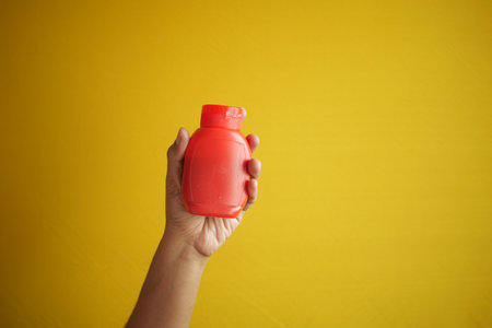 holding a container of chili sauce on yellow backgroundの写真素材