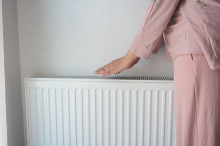 woman warming hands near electric heater at home.の写真素材