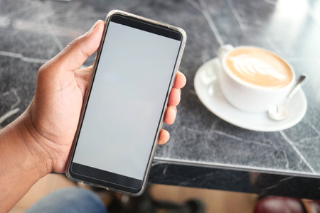hand holding a smart phone with empty screen and coffee on table