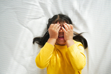 a upset child girl cover her face with hand lying on the bedの写真素材