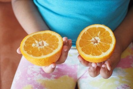 child holding slice of orange fruitの写真素材