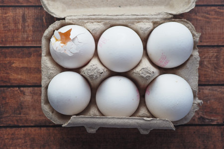 one broken egg with yellow yolk stored in carton container