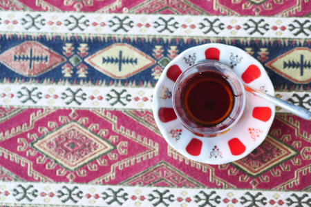 Red Turkish tea with traditional pear shaped glass on patterned tablecloth in cafeの写真素材