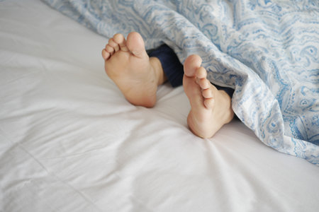 young Woman lying with bare feet in bed,の写真素材