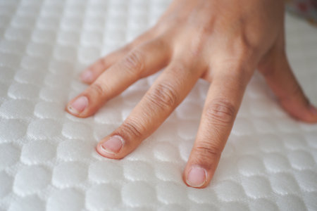 Hand touching and pressing orthopedic mattress on bed.の写真素材