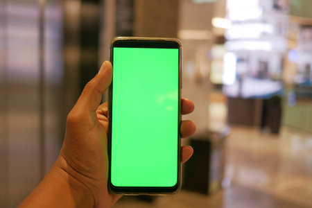 holding smart phone with green screen against shopping mall backgroundの写真素材