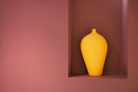 An artifact, a yellow vase, rests in a niche on a pink wallの写真素材