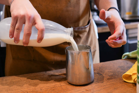 Person pouring milk into a measuring cup on a hardwood tableの写真素材