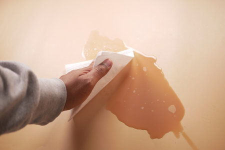hand wiping spilled tea with paper napkin on floor ,