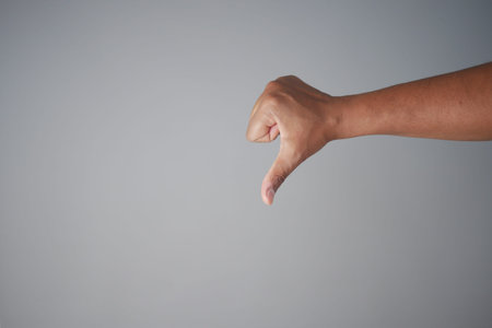 hand showing thumb down sign on gray background.