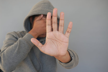 sad man in hood cover face with hands isolated in black.