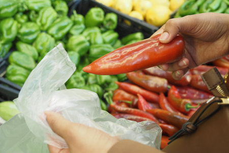woman putting a capsicum in a plastic packet at super storeの写真素材