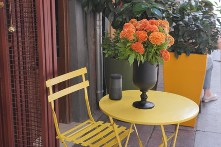 A yellow table in the room with a vase of orange flowers on topの写真素材