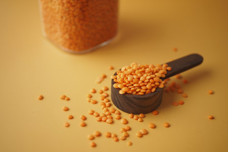 Red lentils in a black scoop on yellow background create a vibrant and wholesome imageの写真素材