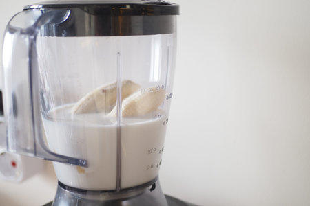 Person making smoothie in blender with food and liquid in kitchen appliance