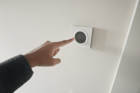 Hand Adjusting Smart Thermostat on White Wall for Optimal Home Temperature Control