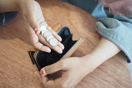 Closeup photo of a female hand holding coins near an open wallet on a wooden table