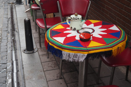 Colorful outdoor cafe scene with a teapot on a patterned table, surrounded by red chairs