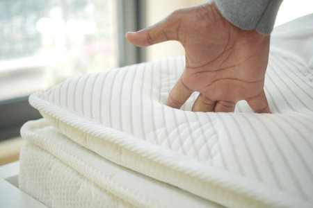 Hand touching and pressing orthopedic mattress on bed.の写真素材