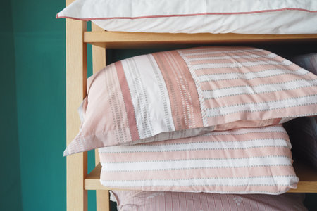 Several comfortable pink and white striped pillows neatly arranged on a wooden shelf in a bedroomの写真素材