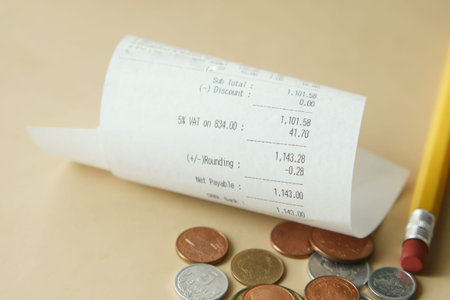 A receipt, coins, and a pencil on a table symbolize finance, transactions, and commerce