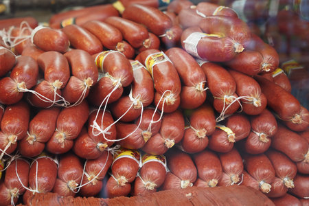 A large stack of deli sausages is on display at a market for sale, tied with stringsの写真素材