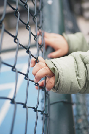 A childs hands gripping a chainlink fence tightly, symbolizing curiosity and exploration in youthの写真素材