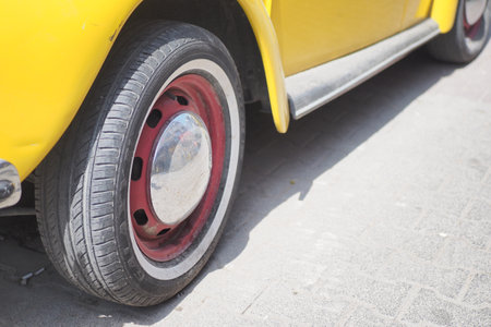 A classic vintage yellow car featuring a striking red accent on its wheel designの写真素材