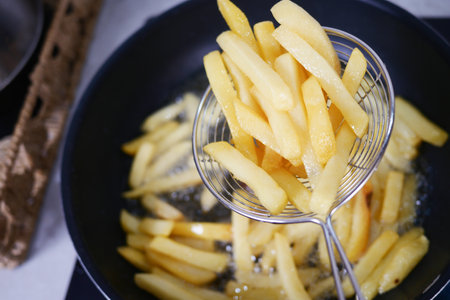 Golden and crispy French fries are being expertly removed from bubbling hot oil as they cookの写真素材