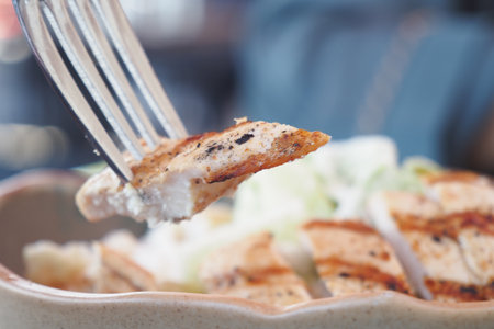 A delicious grilled chicken slice being enjoyed on a fork alongside a fresh, colorful saladの写真素材