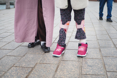 Child cerebral palsy disability with legs orthosis walking outdoor with motherの写真素材