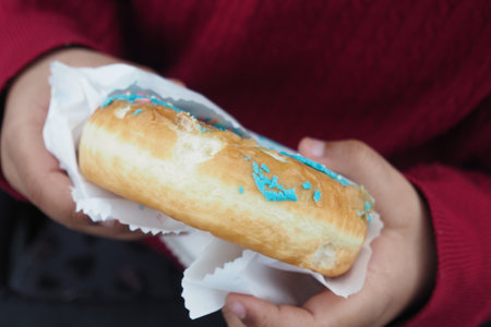A child happily holding a delicious donut topped with colorful blue sprinkles in their handsの写真素材