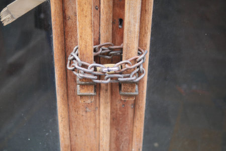A set of locked wooden doors secured with a robust chain and a sturdy padlock for safetyの写真素材
