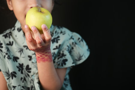 A child joyfully holds a bright green apple, showcasing innocence and henna artの写真素材