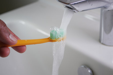 slow motion of holding toothbrush under flowing water in bathroom, closeup.の写真素材