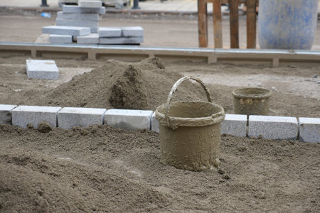 A bustling construction site showcasing buckets and bricks situated on a sandy ground surfaceの写真素材