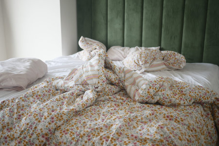 A disheveled bed adorned with vibrant, colorful floral bedding and a striking green headboard