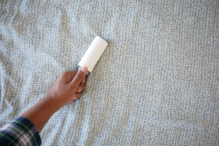 using an adhesive roller to remove lint and fluff from a bed .の写真素材