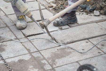 A construction worker is currently using an electric jackhammer to break up pavement tiles