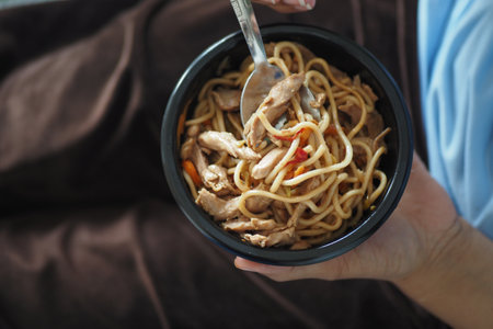 A bowl of delicious chicken noodles rests on a cozy blanket, with a fork beside itの写真素材
