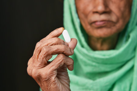 An Elderly Woman Carefully Holding a Pill with Great Care and Attention to Detailの写真素材