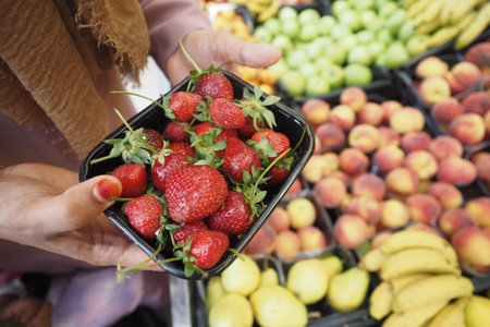 Close up of hands taking small plastic box of fresh strawberries in store..の写真素材
