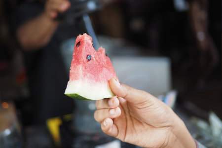 A Fresh Slice of Watermelon Being Held by a Hand Set Against a Vibrant and Lively Backgroundの写真素材