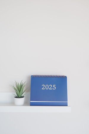 A Minimalistic Desk Setup featuring a 2025 Calendar along with a Potted Plant for ambianceの写真素材