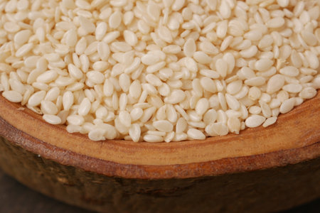 A closeup image showing raw white sesame seeds neatly displayed in a rustic wooden bowlの写真素材